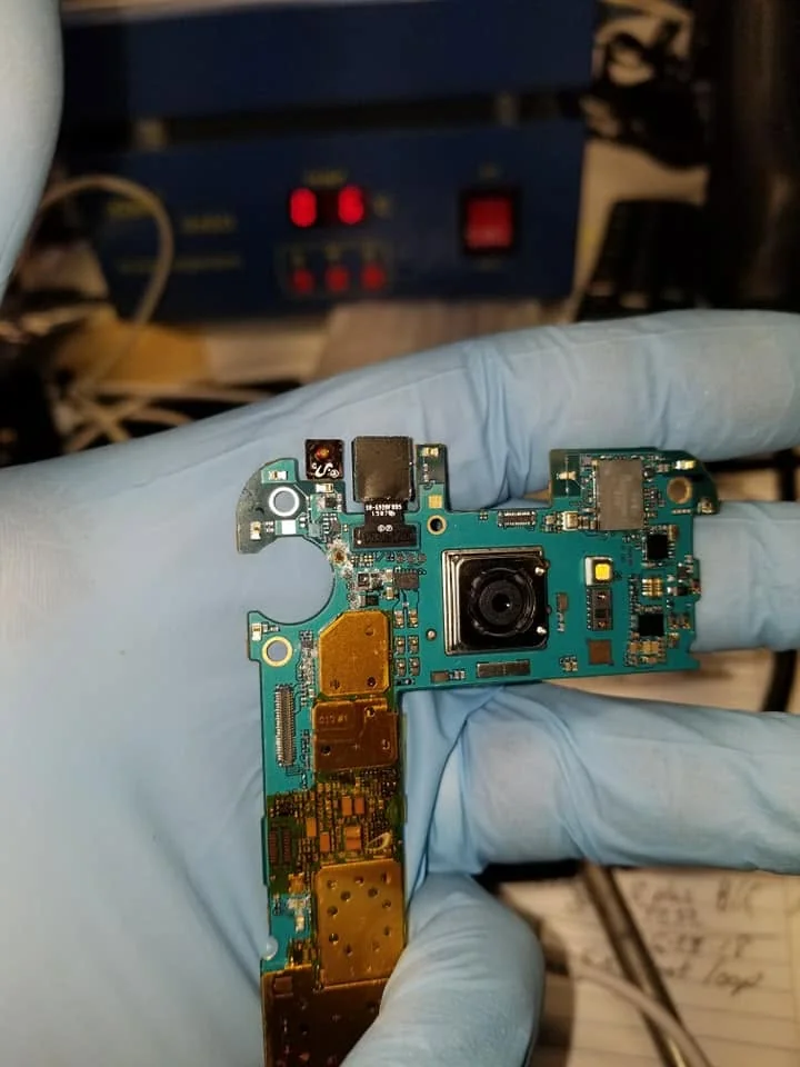 Smartphone motherboard being repaired under magnification